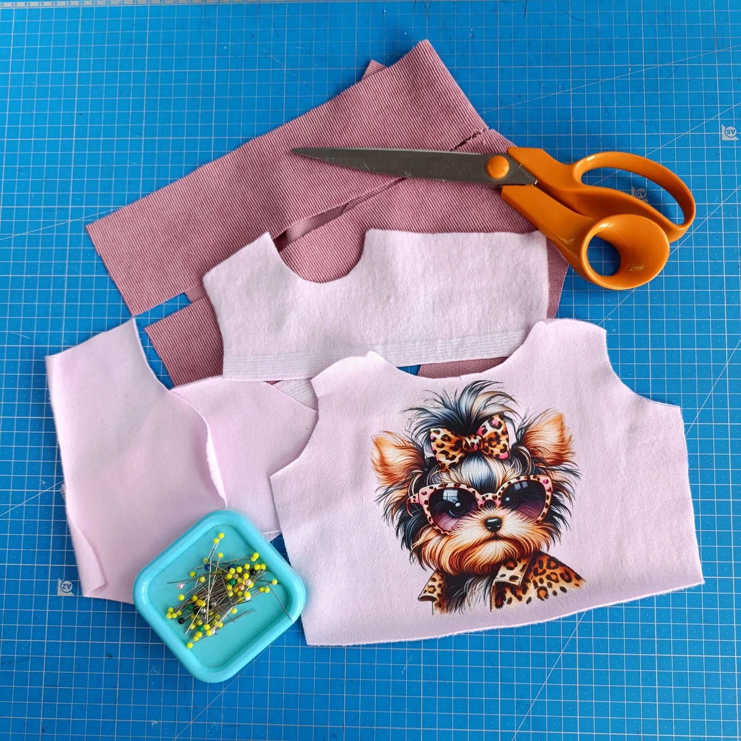 Fabric pieces with a dog design, scissors, and pins on a blue cutting mat.