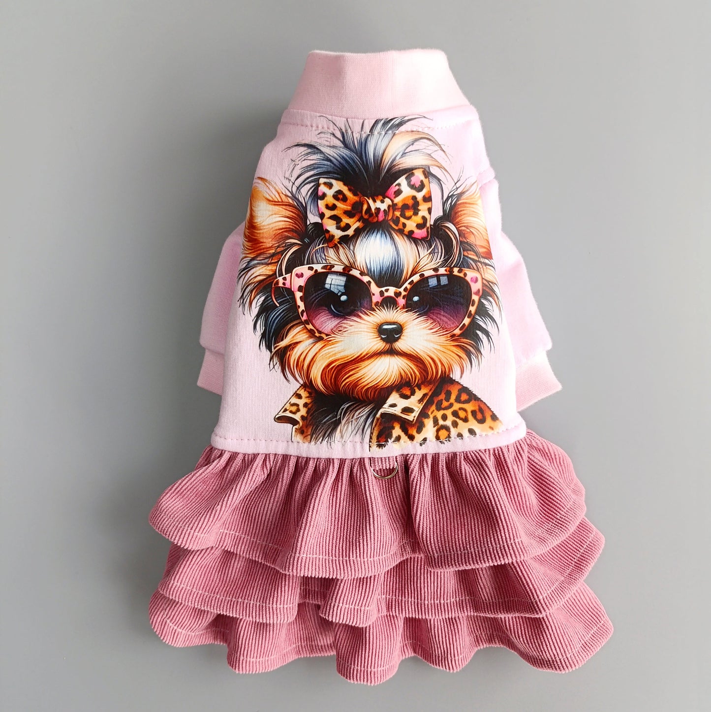 Flat lay of pink dog outfit with ruffle skirt and illustrated Yorkie with bow and sunglasses.